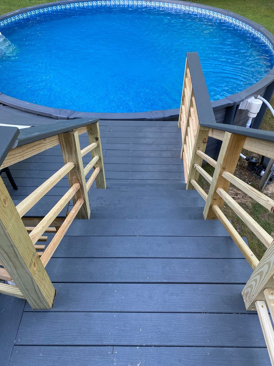 Wooden stairs leading down to a bright blue round pool with a deck railing on both sides