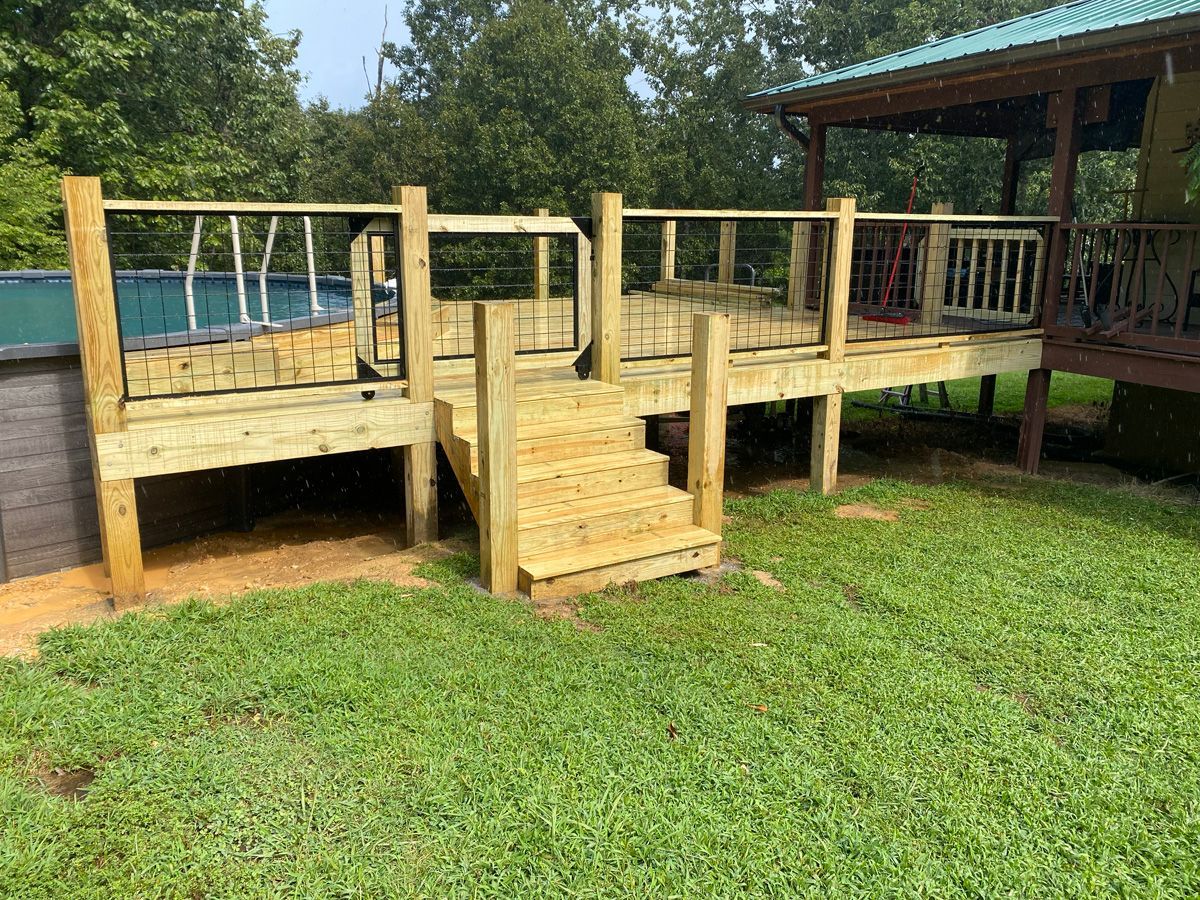 Wooden deck with railing and steps beside a grassy yard and covered patio by the water