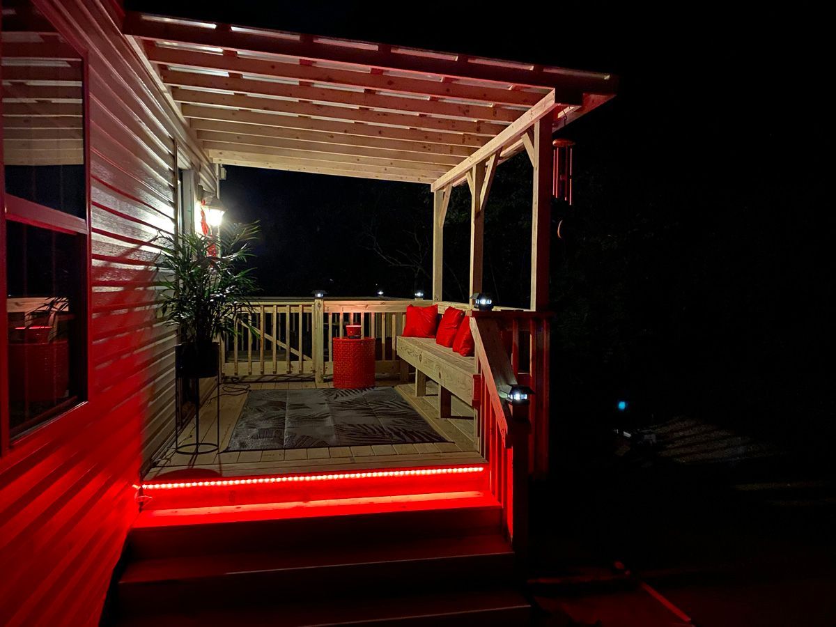 Red-lit wooden deck at night with porch seating, railing, and a potted plant