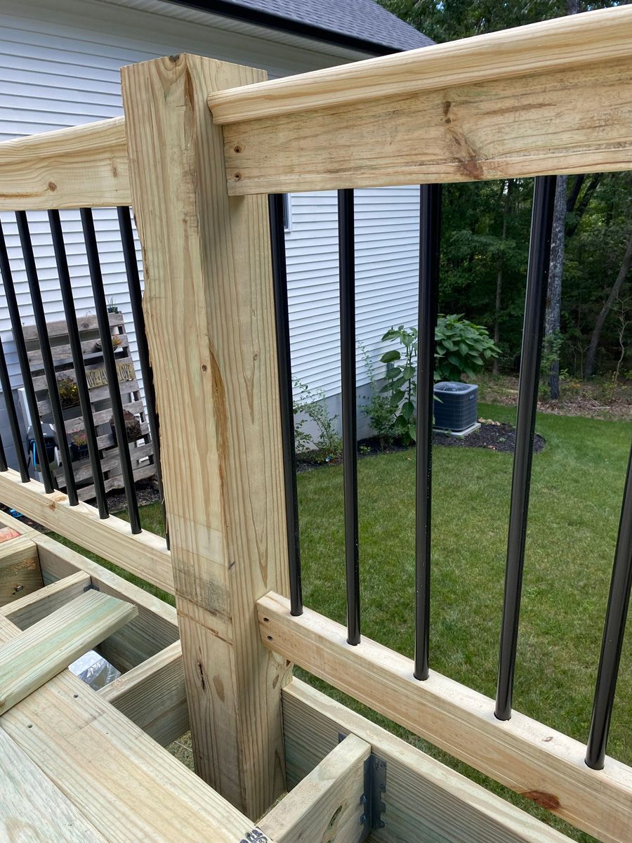 Wooden deck railing under construction with black balusters and a backyard lawn beyond.