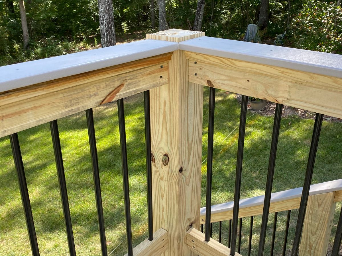 Wooden deck railing corner with white cap and black balusters overlooking a grassy yard