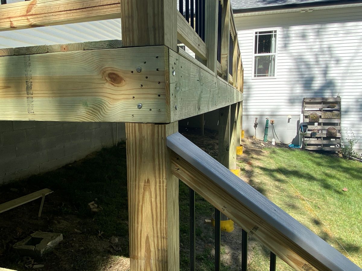 Wooden deck corner with support post and black railing beside a grassy yard and house siding
