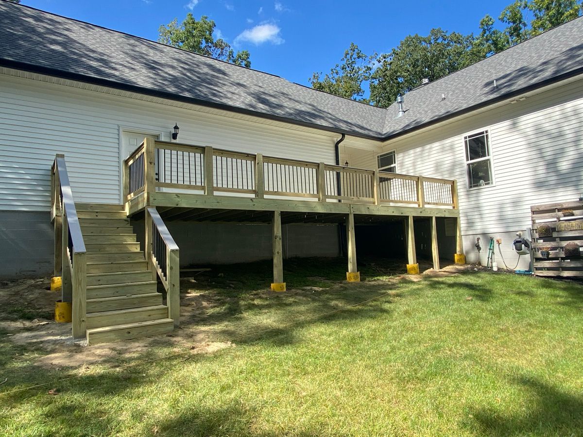 Raised wooden deck and stairs attached to a white house in a grassy backyard