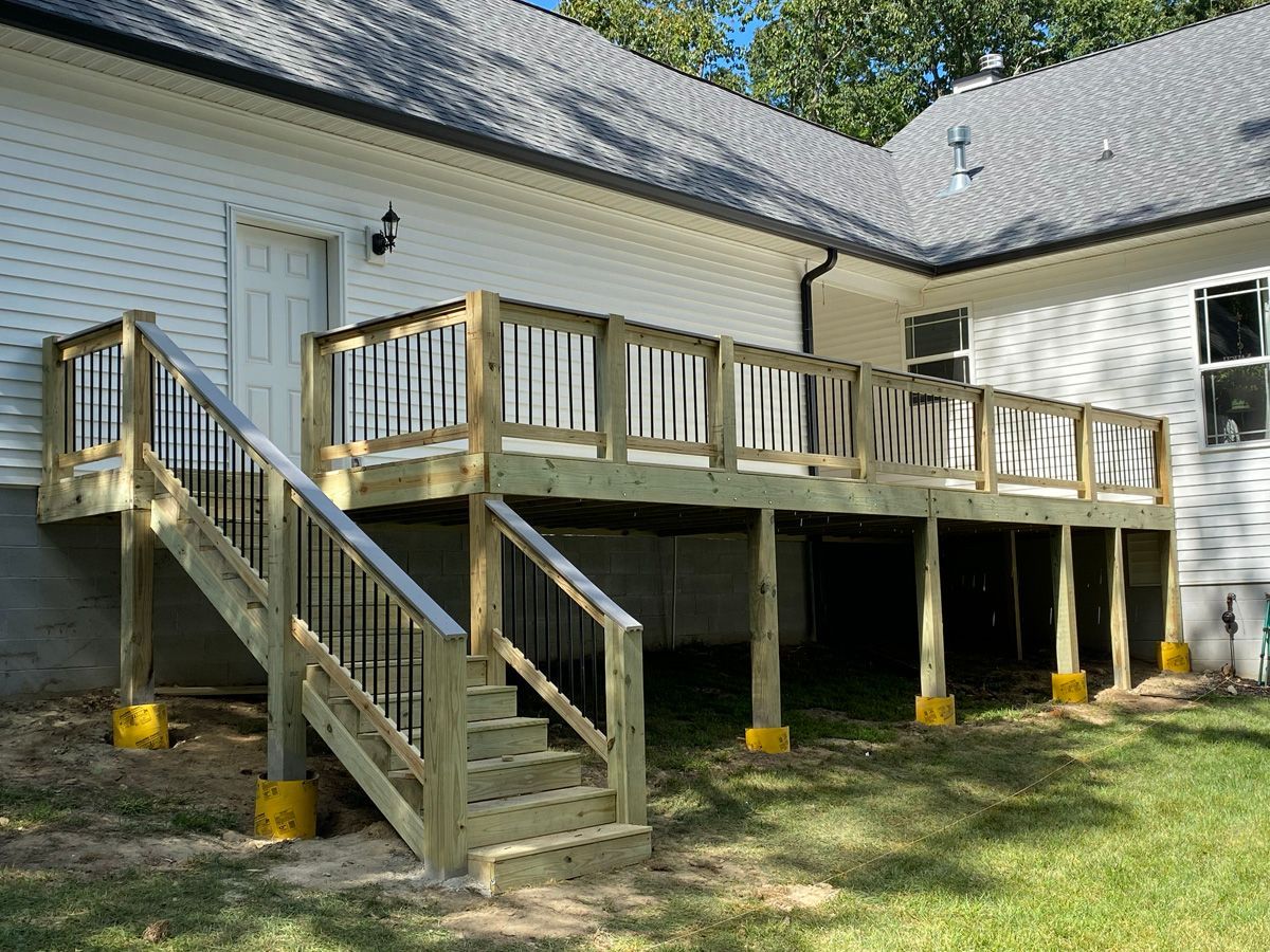 Wooden deck with stairs attached to a white house, supported by posts over a grassy yard