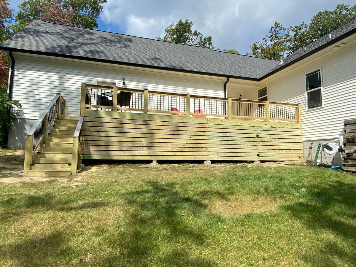 Backyard deck with wooden stairs, white house siding, and grassy lawn under a partly cloudy sky