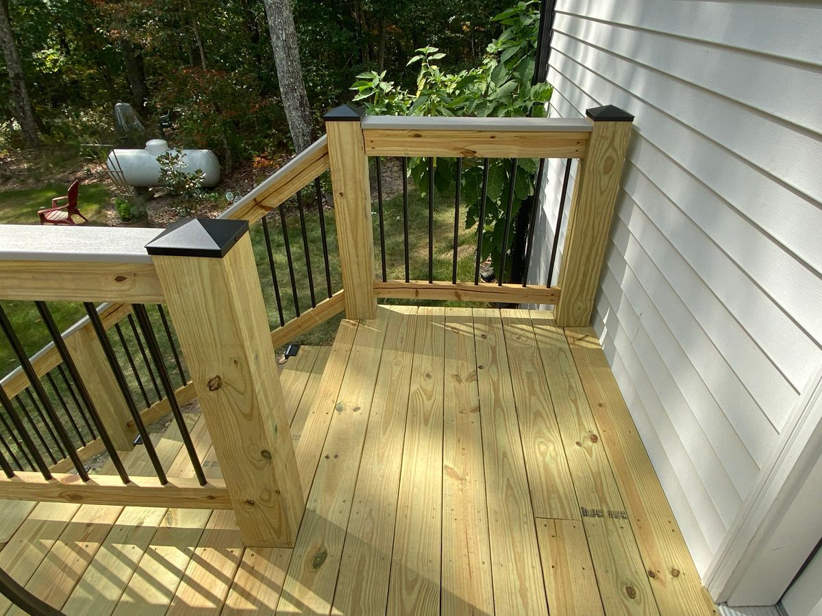 Wooden backyard deck with railing, stairs, and a white house wall beside it