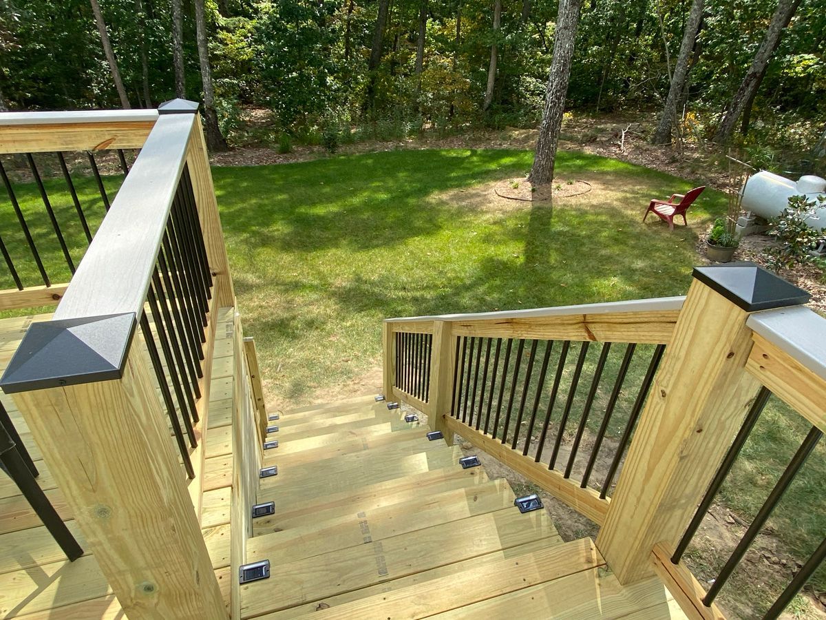 Wooden outdoor stairs descending to a grassy yard surrounded by trees and black railings
