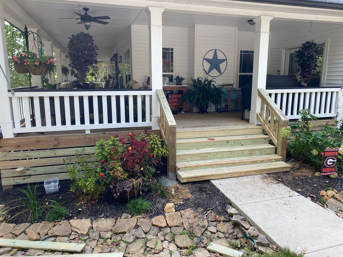 Front porch with white railings, wooden steps, potted plants, and a star wall decoration.