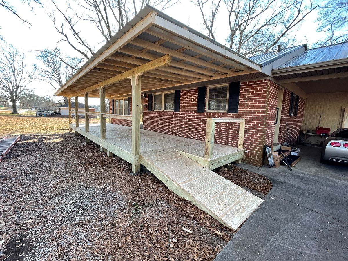 Covered wooden ramp leading to a brick house entrance beside a driveway and carport