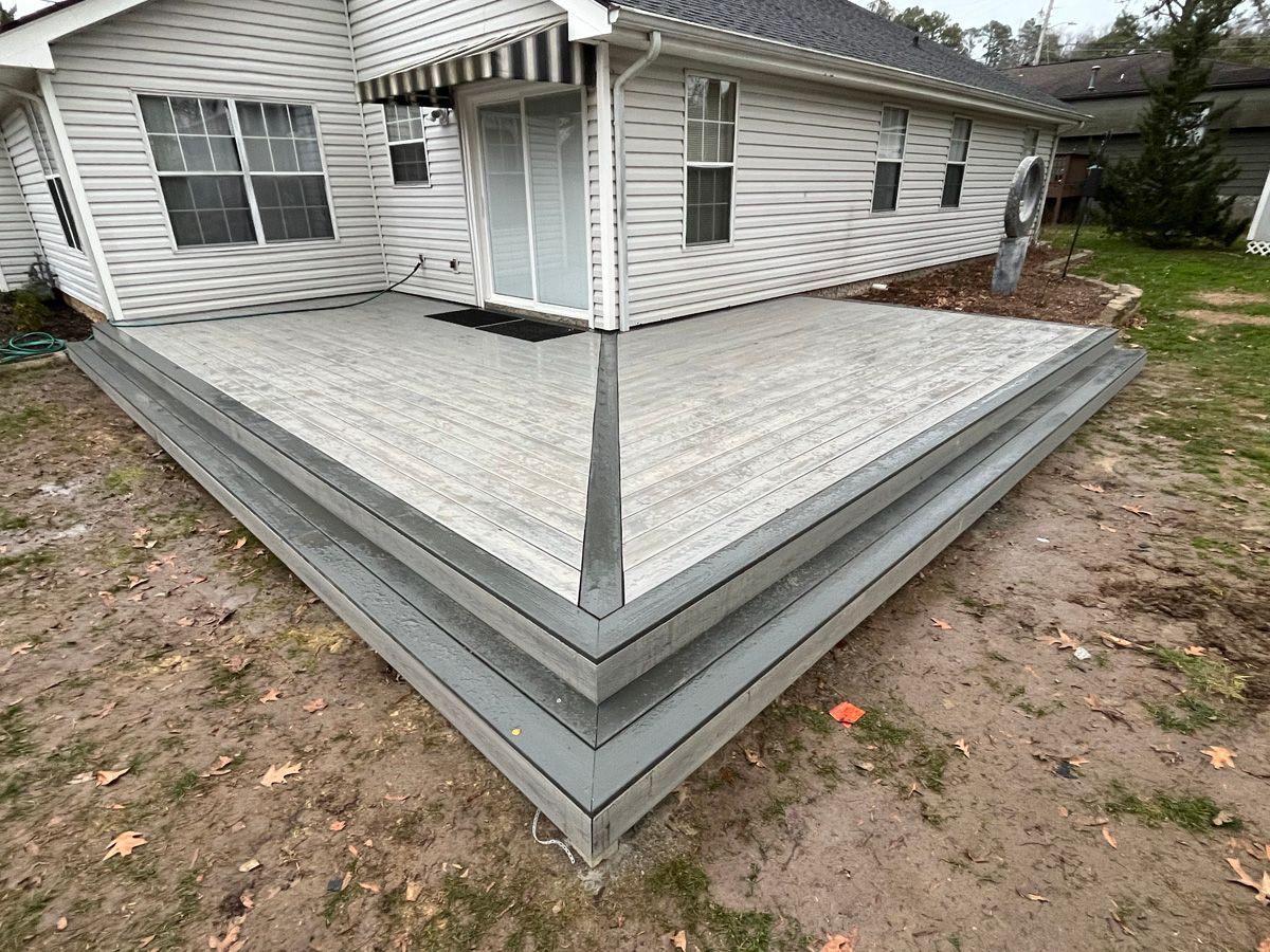 Weathered gray wooden deck wrapping a white house, viewed from the corner in a yard.