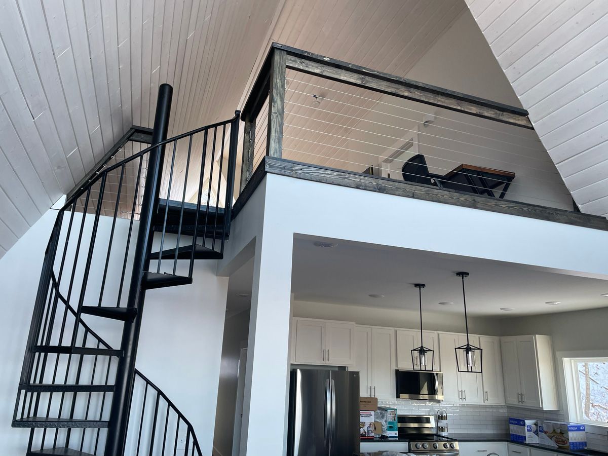 Spiral staircase beside a lofted bed above a modern kitchen in a bright open apartment.