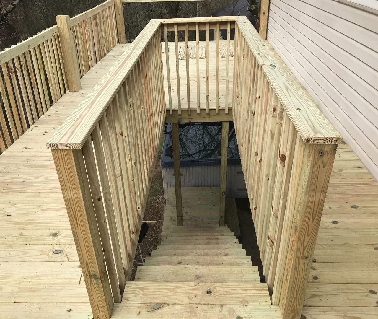 Wooden stairwell opening between deck railings on a light wood deck, viewed from above
