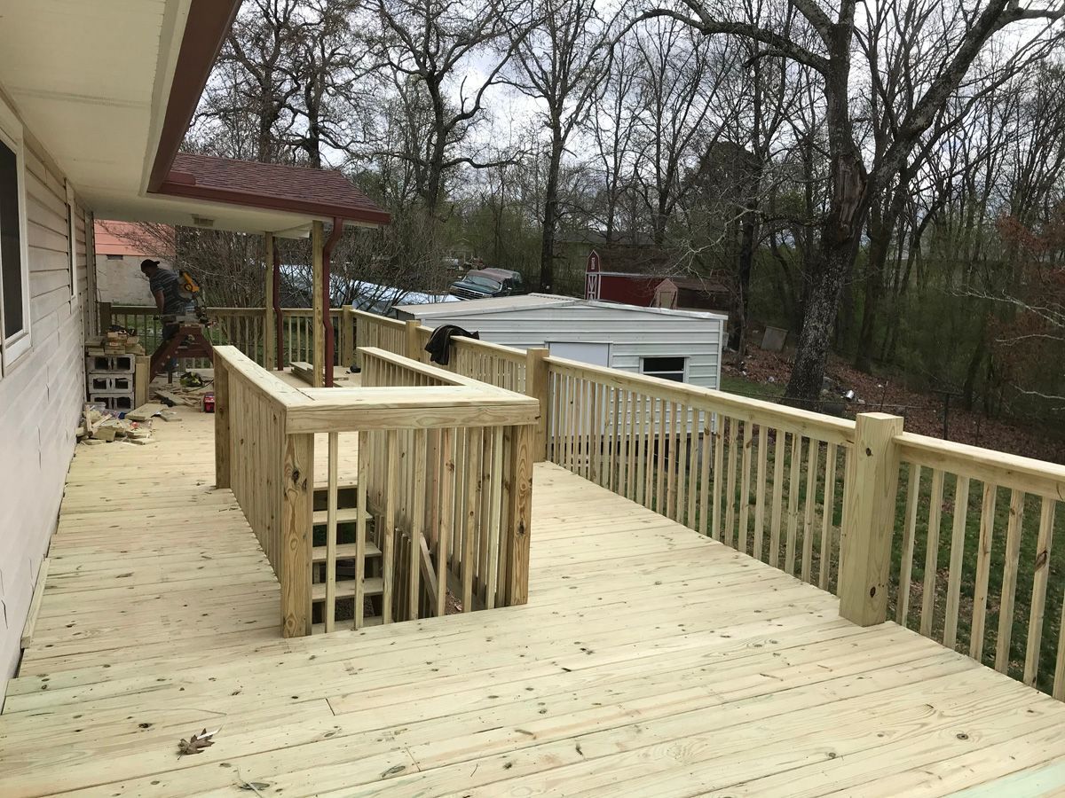 Wooden deck with railings and steps beside a house, overlooking a wooded yard