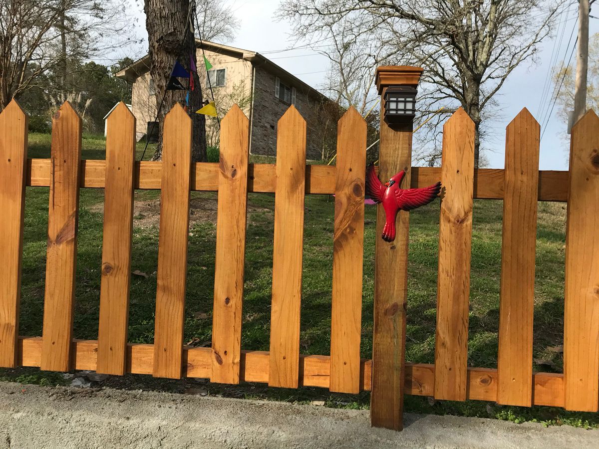 Wooden picket fence with orange posts and a red ribbon tied to one post, in a grassy yard