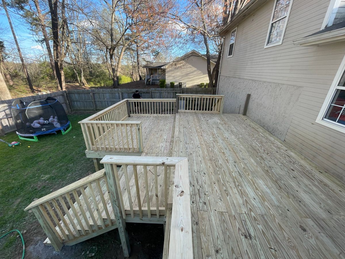 Wooden backyard deck with stairs, railing, and adjacent house wall in fall foliage