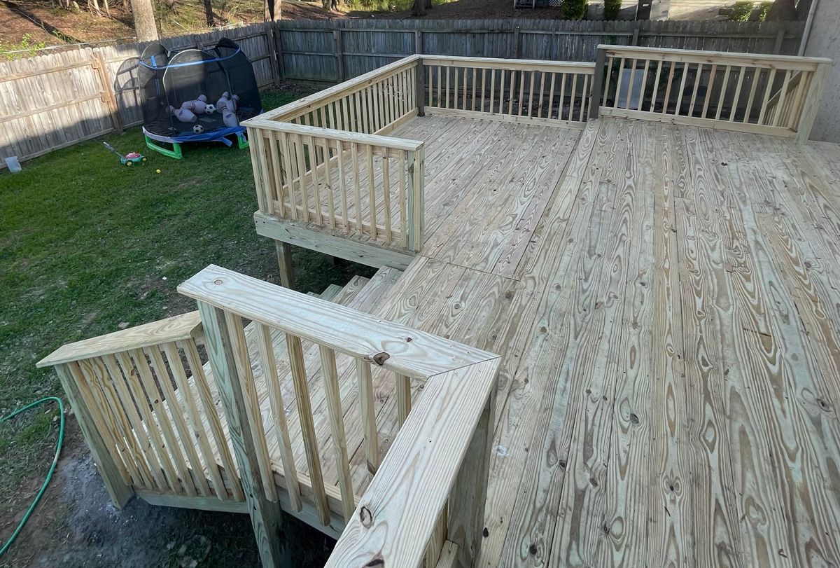 Wooden backyard deck with stairs, railings, and a small upper platform beside a grassy yard.