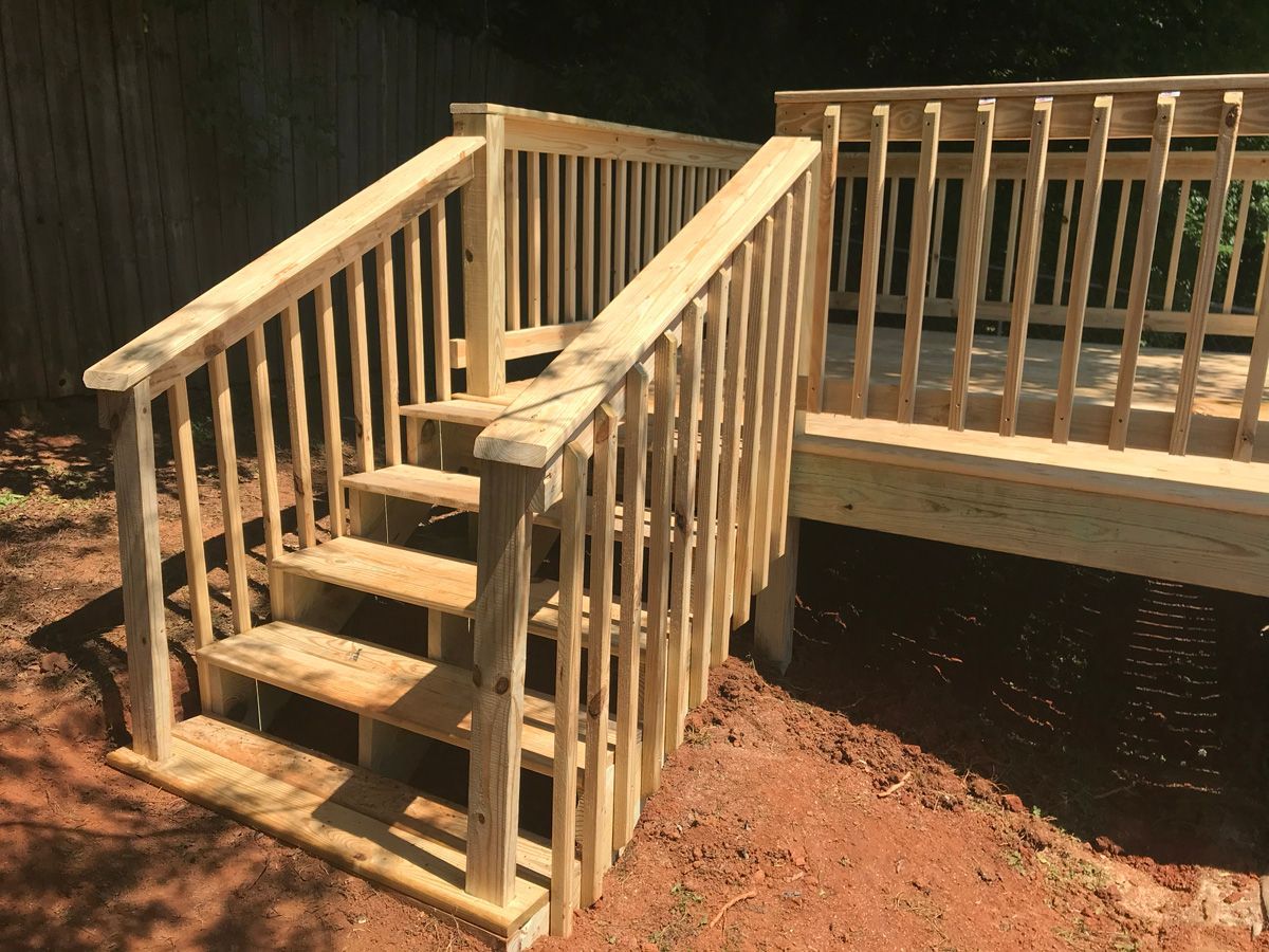 Wooden deck stairs with a handrail leading down to a dirt yard beside a raised porch