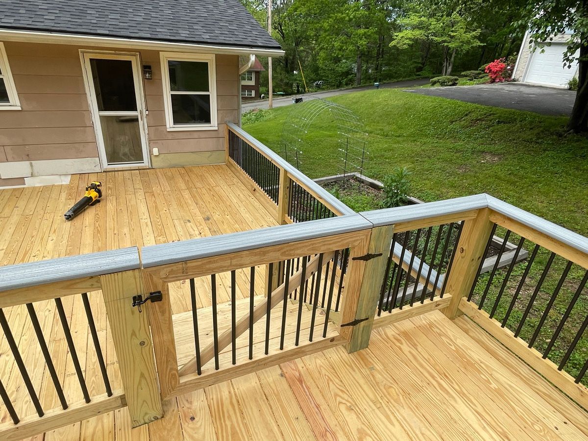 Wooden deck and railing beside a house, with tools on the deck and a grassy yard beyond.