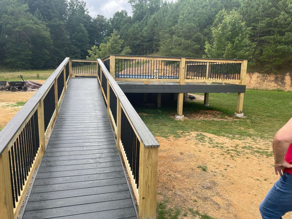 Accessible wooden bridge leading to a raised viewing deck over a sandy clearing with trees beyond