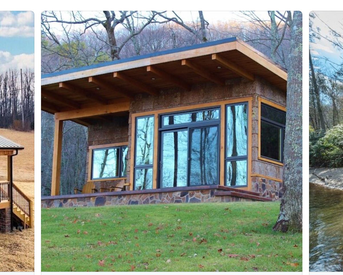 Small modern cabin with wood siding, large glass doors, and a slanted roof on a grassy hillside.