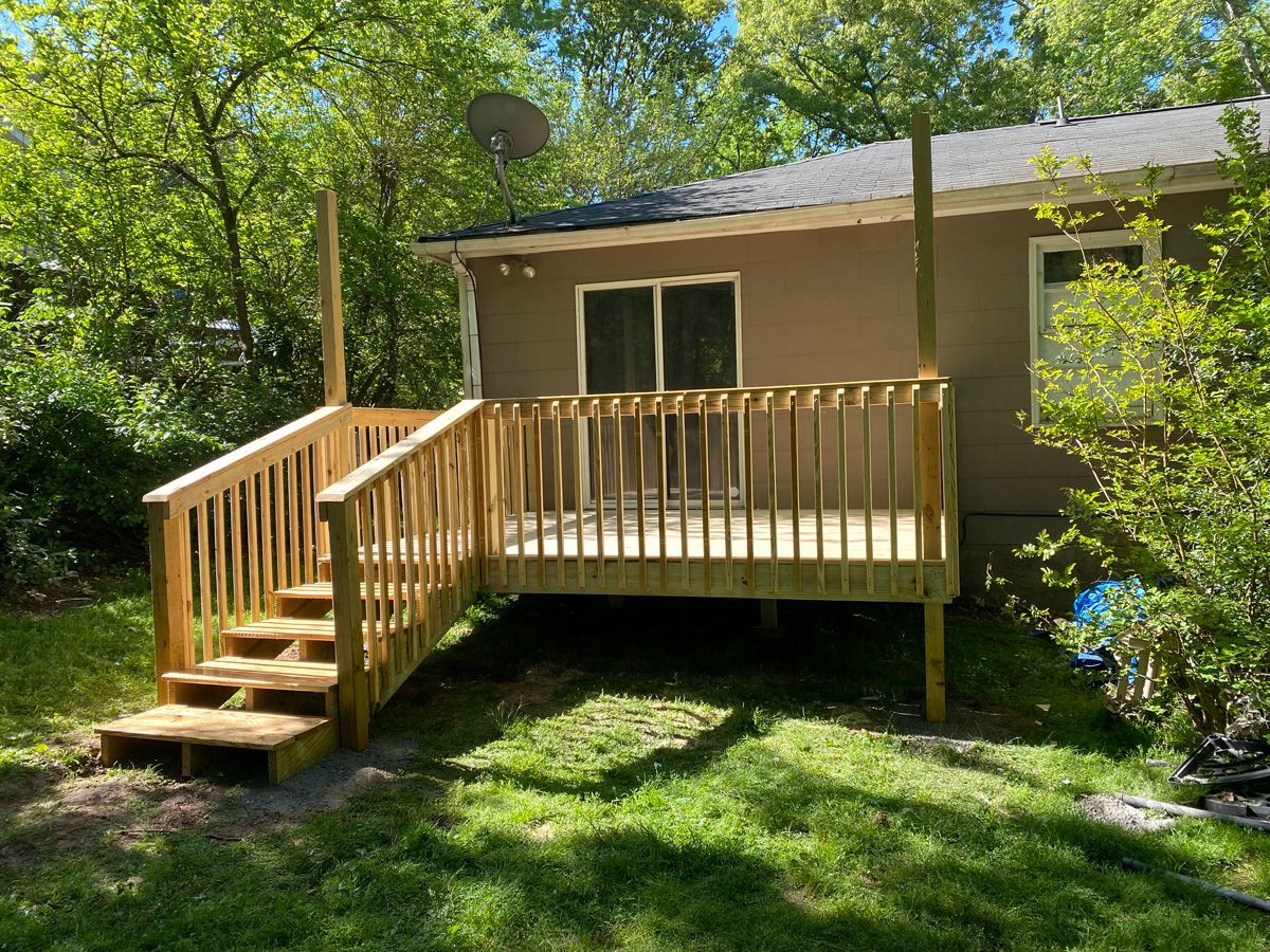 Wooden deck and stairs attached to a small house in a leafy backyard