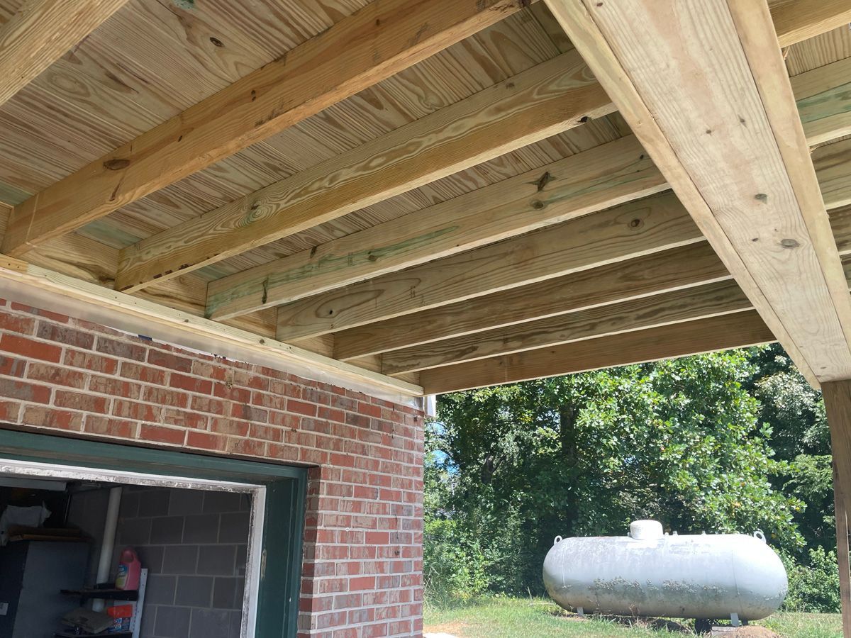 Wooden deck framing over a brick garage with an open doorway and a white propane tank in the yard