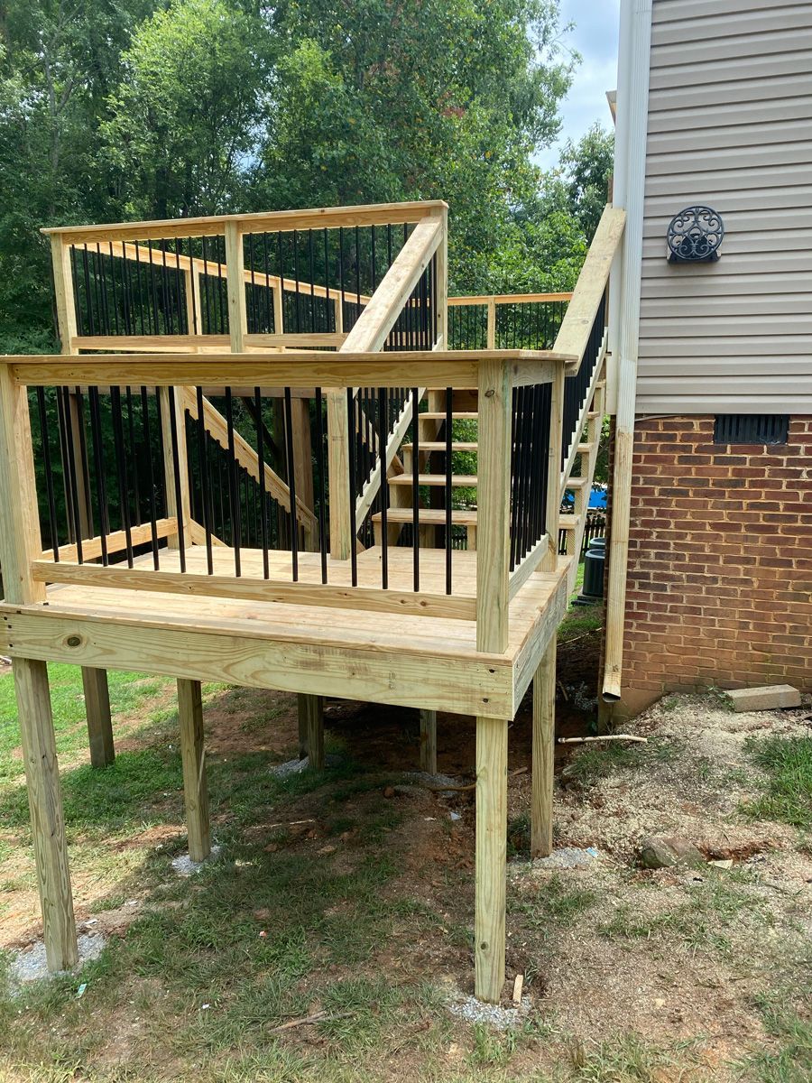 Raised wooden deck under construction beside a brick house, with unfinished railings and stairs.