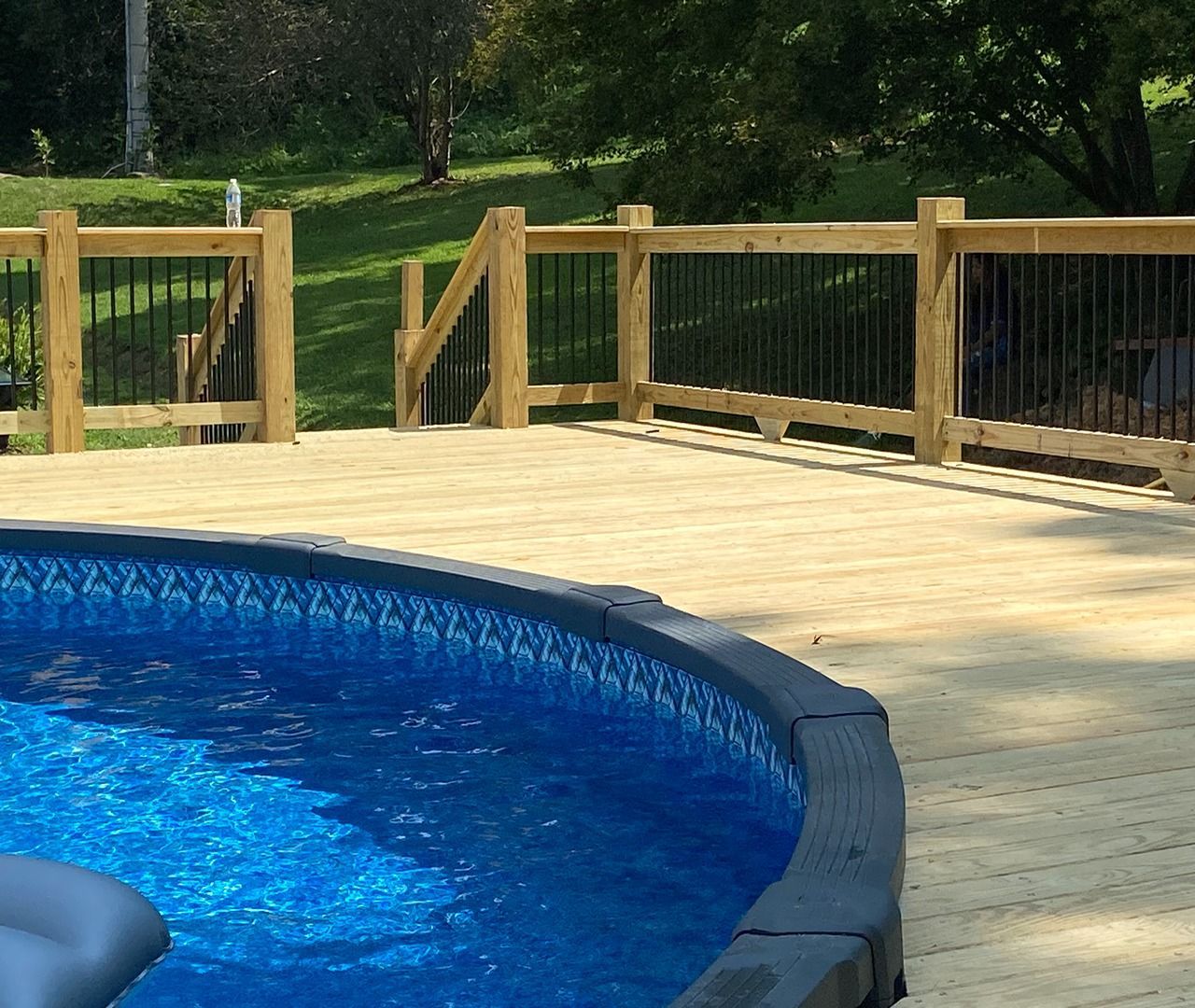 Blue swimming pool beside a wooden deck and fence in a sunny backyard