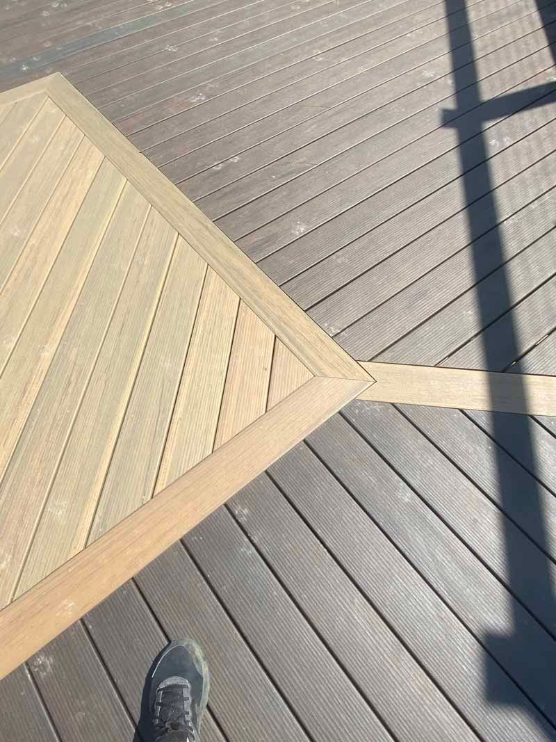 Wooden ramp or deck corner on a gray boardwalk, with a shoe visible at the bottom edge.