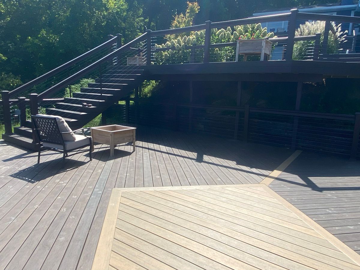 Wooden deck with stairs, lounge chair, small table, and shaded outdoor seating area under trees