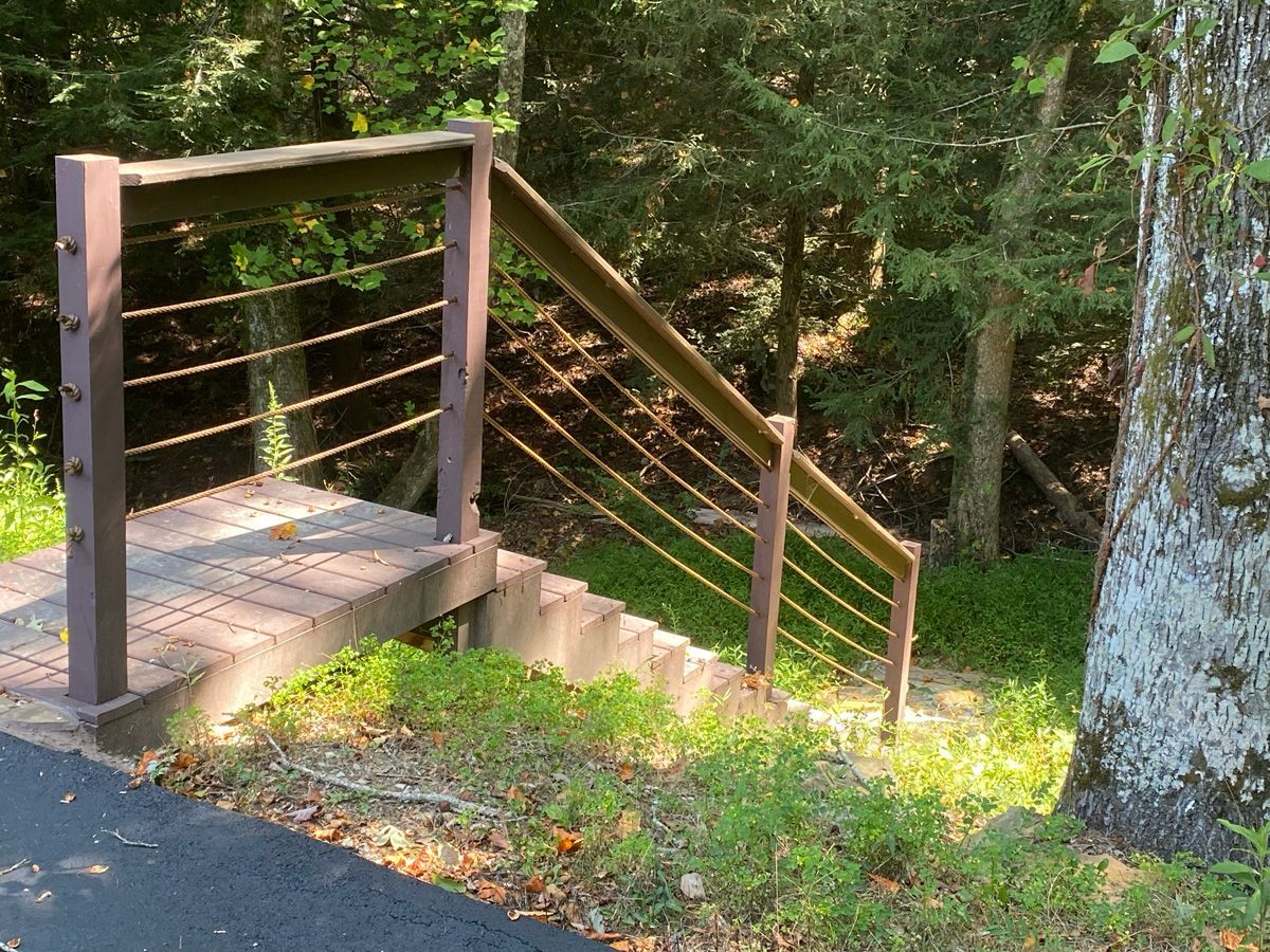 Wooden outdoor staircase and railing descending a wooded hillside beside a paved path