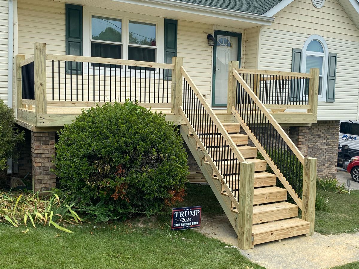 House with front porch and wheelchair ramp leading up steps, beside bushes and a small yard sign.