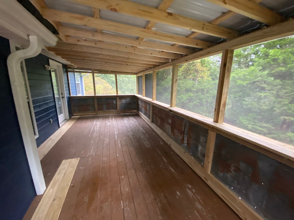 Empty covered wooden porch with screened railings and exposed beams, overlooking trees