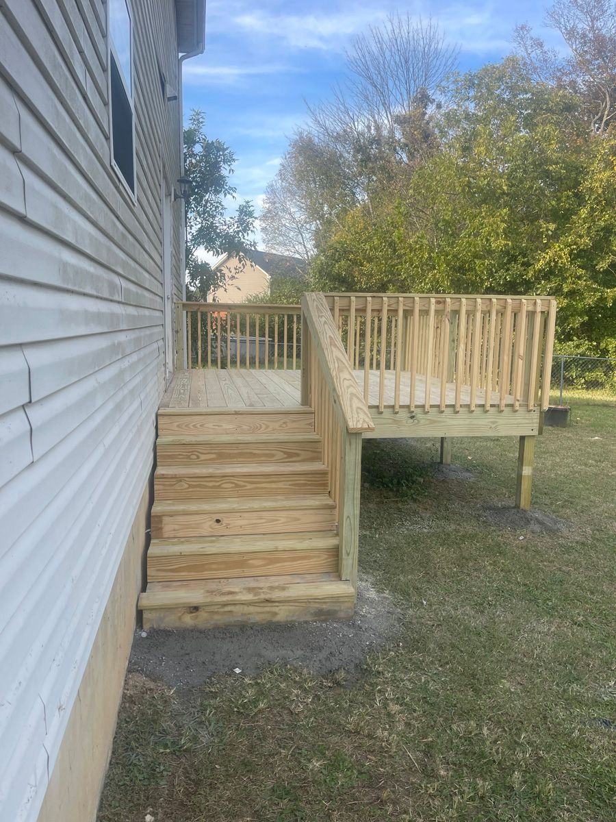 Wooden backyard deck with steps beside a house, bordered by a railing and set on grass.