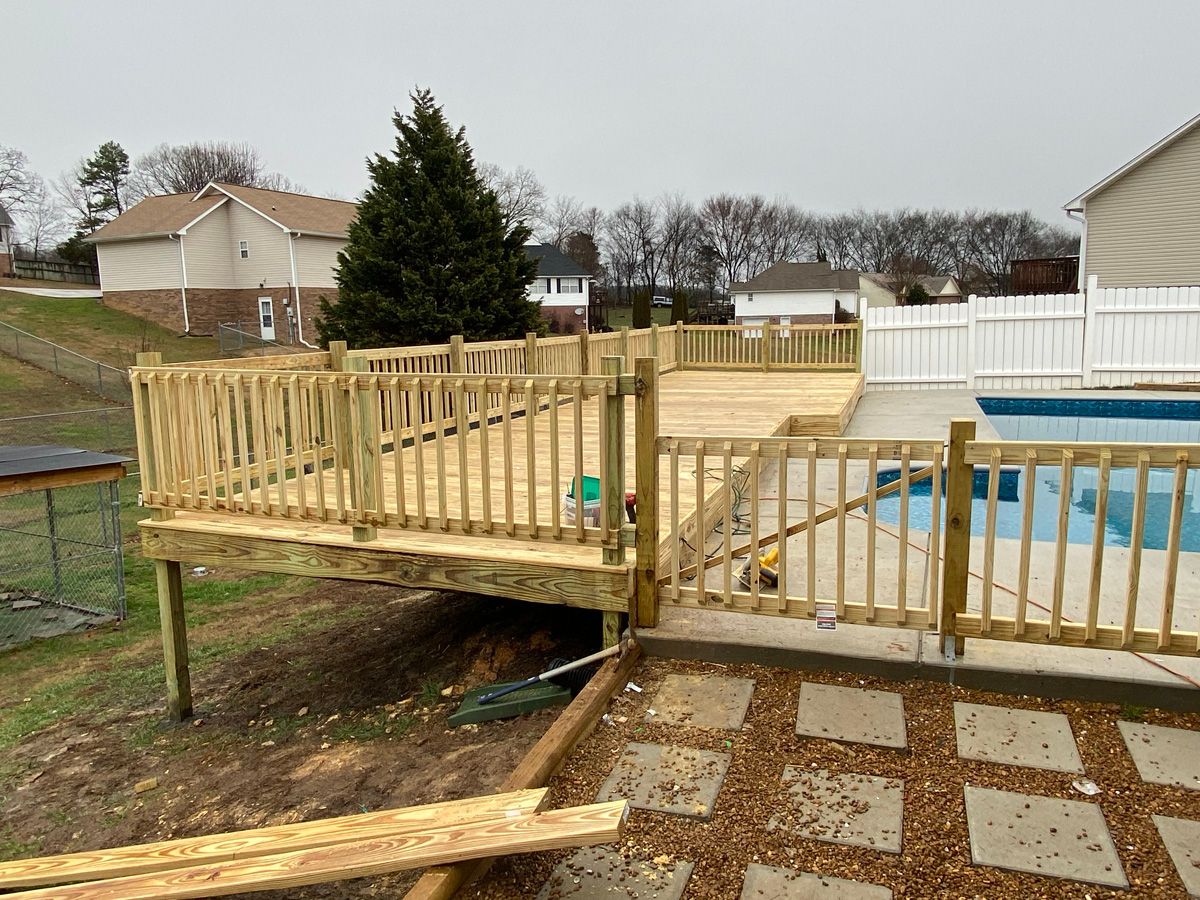 Wooden pool deck ramp with railings beside an above-ground pool in a backyard