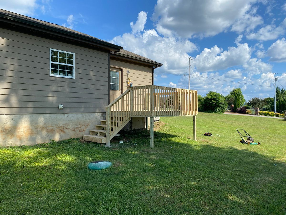 House with small wooden deck and stairs in a grassy yard under a blue sky