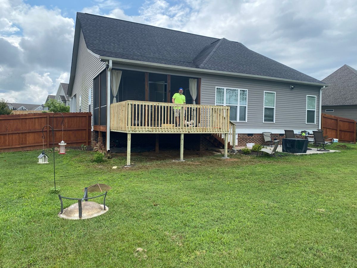 House with a small wooden deck under construction in a grassy backyard; person in neon shirt on the deck