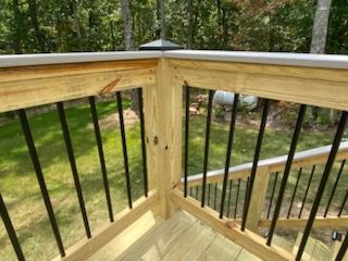 Wooden deck corner with black metal balusters overlooking a grassy yard and trees