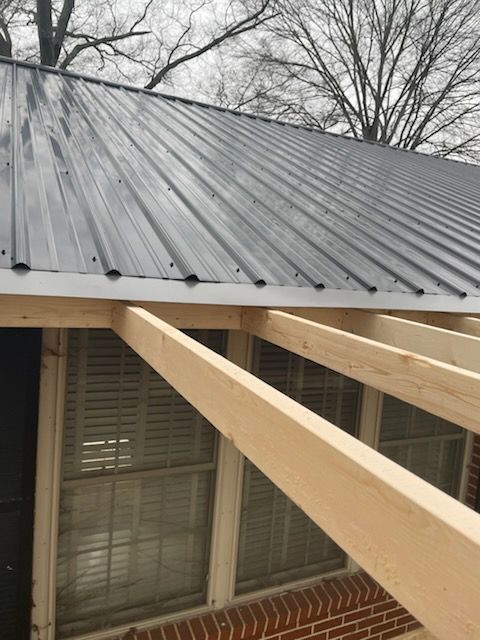 Metal roof over porch with exposed wooden beams above a house window.