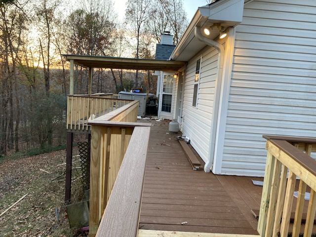 Wooden deck walkway beside a white house, overlooking a wooded hillside at sunset