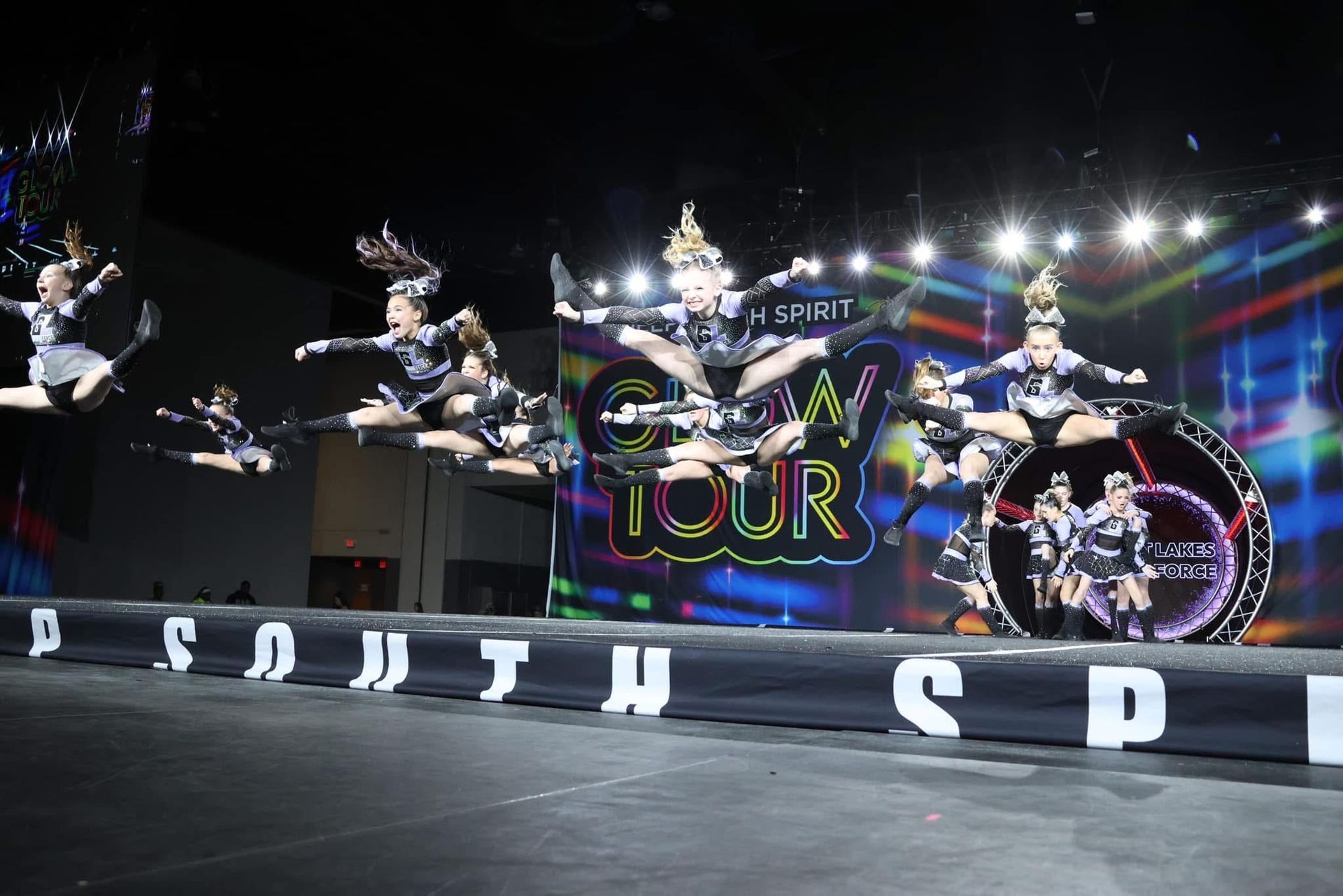 A group of cheerleaders are jumping in the air on a stage.
