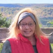 A woman wearing glasses and a red vest is smiling for the camera.