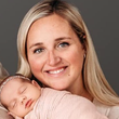 A woman is holding a baby wrapped in a pink blanket.