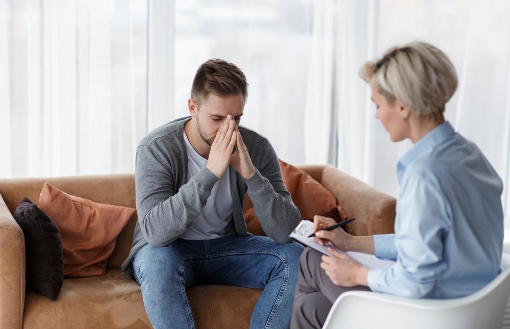 Man With Hands Covering Face on Couch — AT My Place Counselling and Psychotherapy in Neutral Bay, NSW