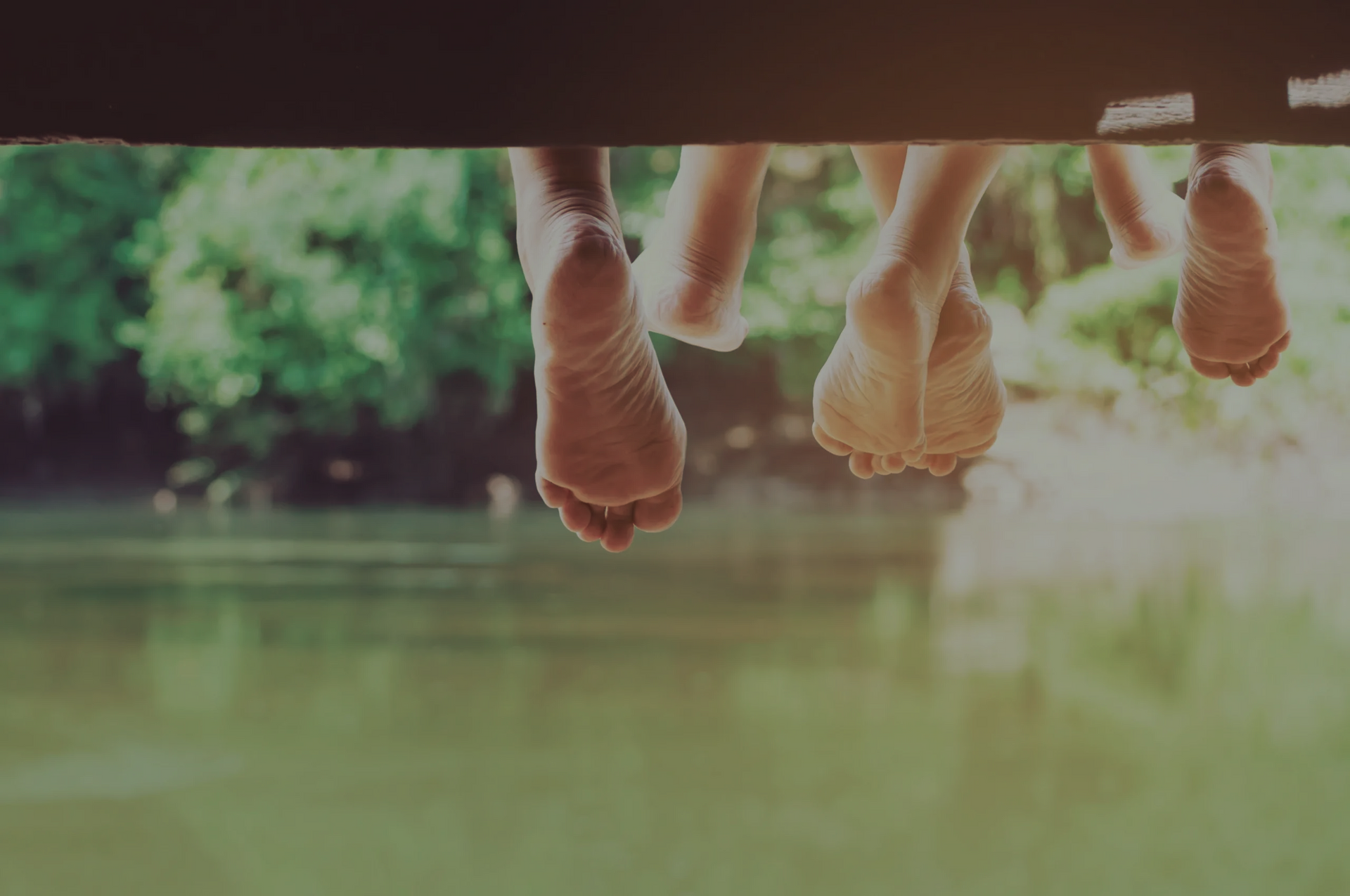 Bare feet dangling from wooden dock over water; green trees in background. — AT My Place Counselling and Psychotherapy in Mosman, NSW