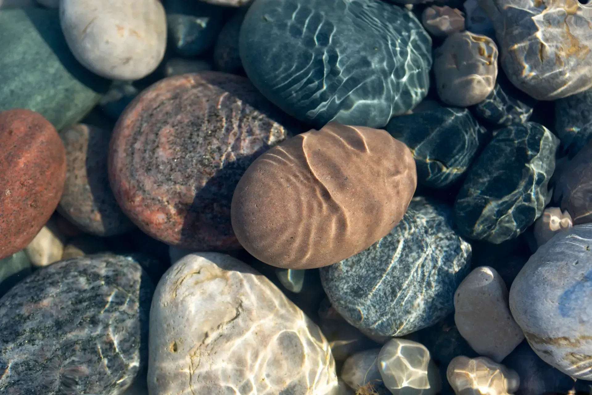 Rounded, colourful rocks submerged in clear water, with light reflections. — AT My Place Counselling and Psychotherapy in Neutral Bay, NSW