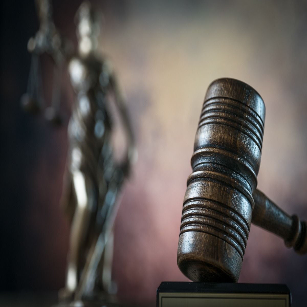 There is a statue of justice in the background and a wooden gavel in the foreground.