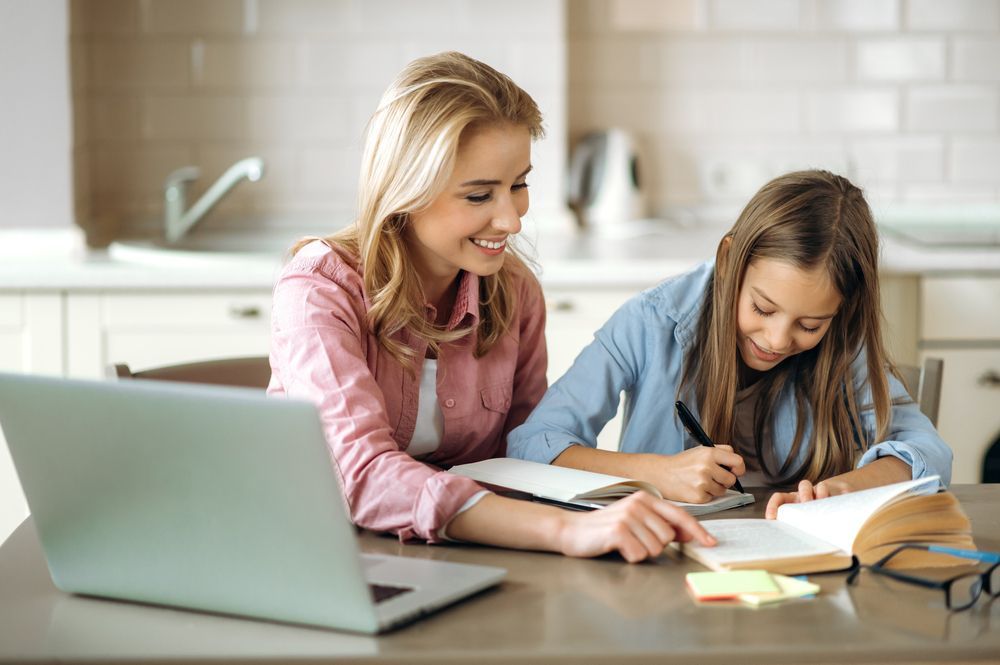 Woman Helps Girl With Homework at a Kitchen Table; a Laptop Sits Nearby — Shane Kelly Communications in Lennox Head, NSW