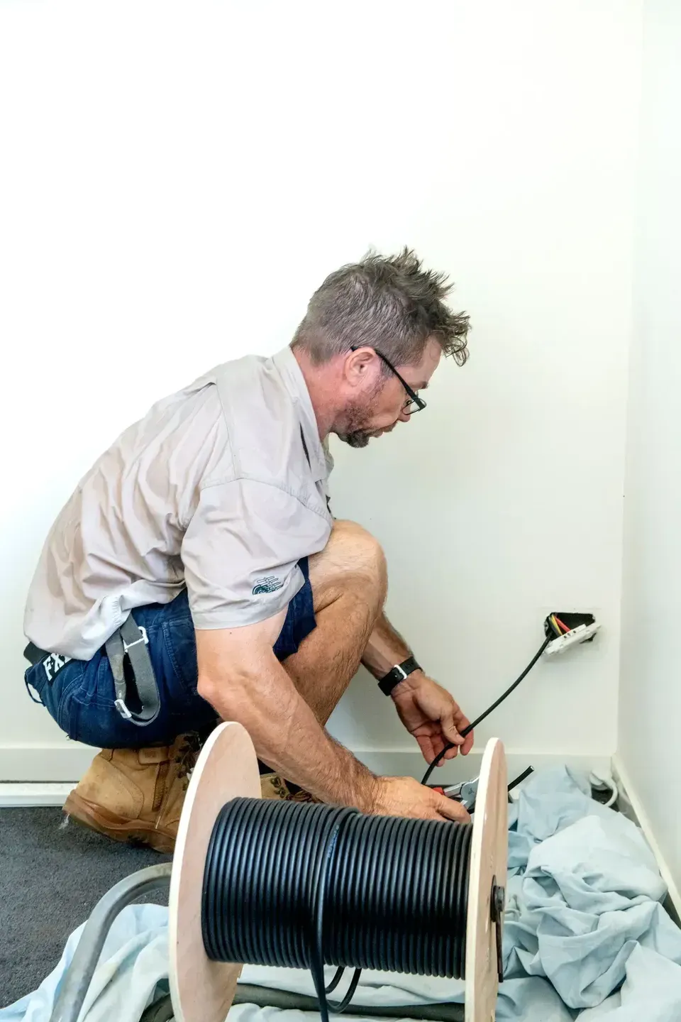 A Man Installing a Cable, Squatting Near an Electrical Outlet — Shane Kelly Communications in Lennox Head, NSW