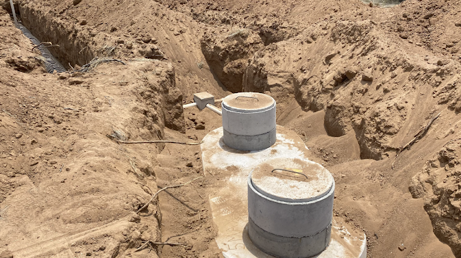 Two gray pipes protrude from a sandy trench at a construction site.